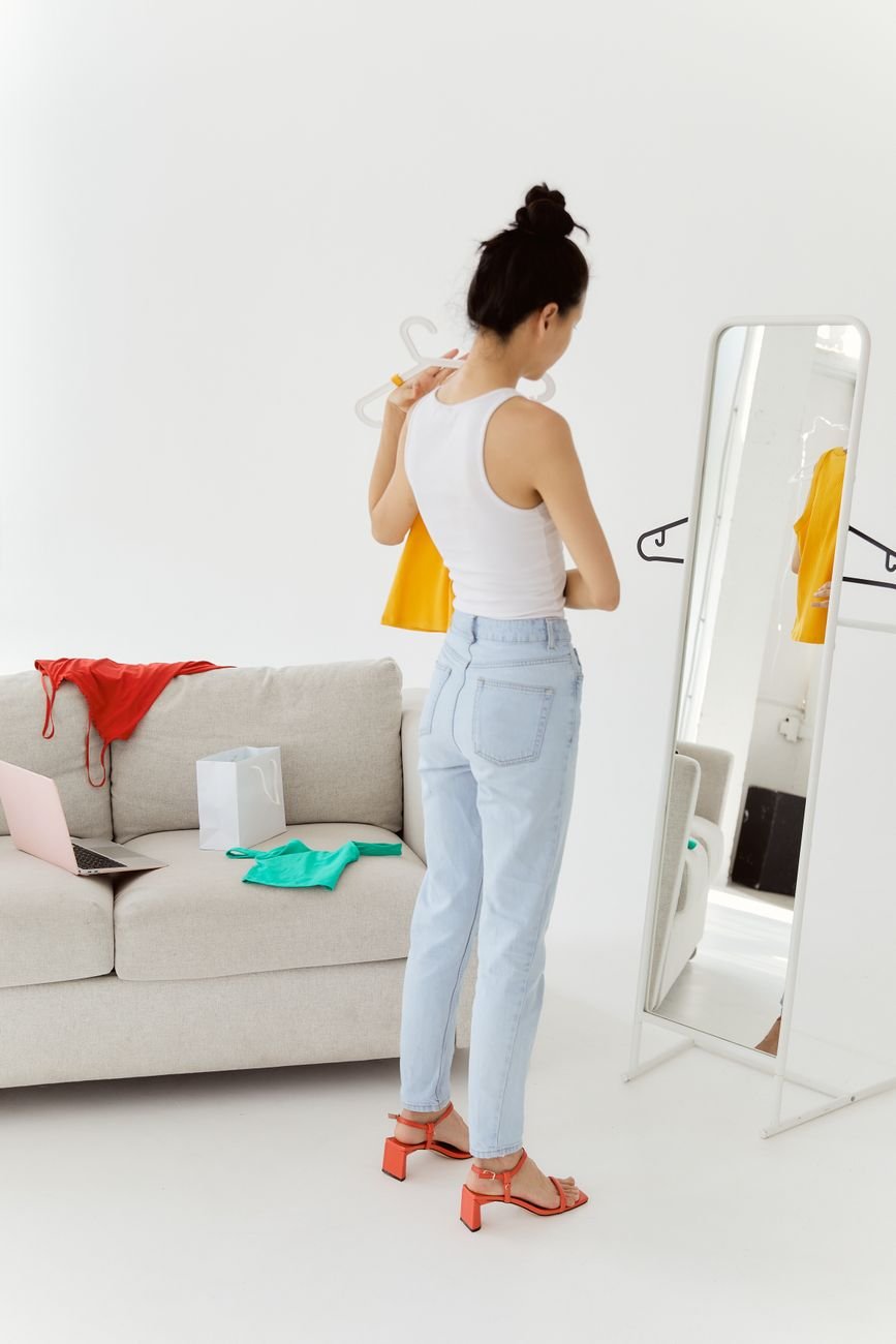 Young woman choosing outfit in stylish modern living room with mirror.